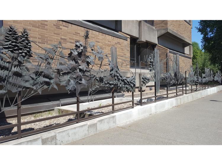 A section of the sculpture, depicting leafy vegetation and outlines of mountains, is seen at an angle