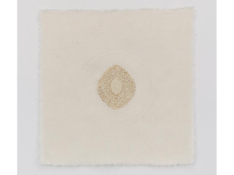 Stiched artwork with a small oval-shaped area of gold and white stitching at center, on off-white background
