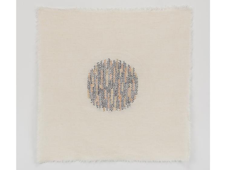 Stiched artwork with a small round area of blue, orange and gold stitching at center, on off-white background