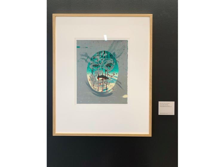 The artwork is shown framed and hung on a dark grey wall, with a small descriptive plaque next to it