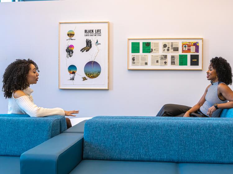 Image of two people seated with 2 framed artwork in the background