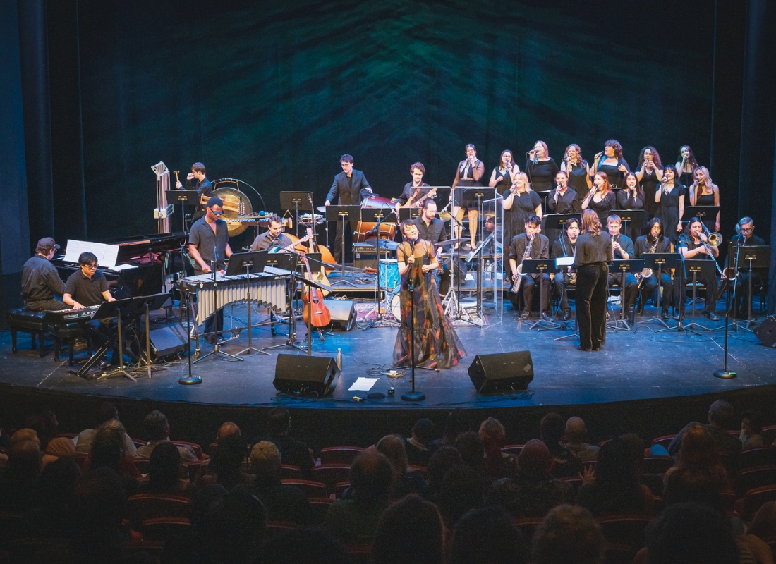 A jazz big band with musicians and singers perform on stage.