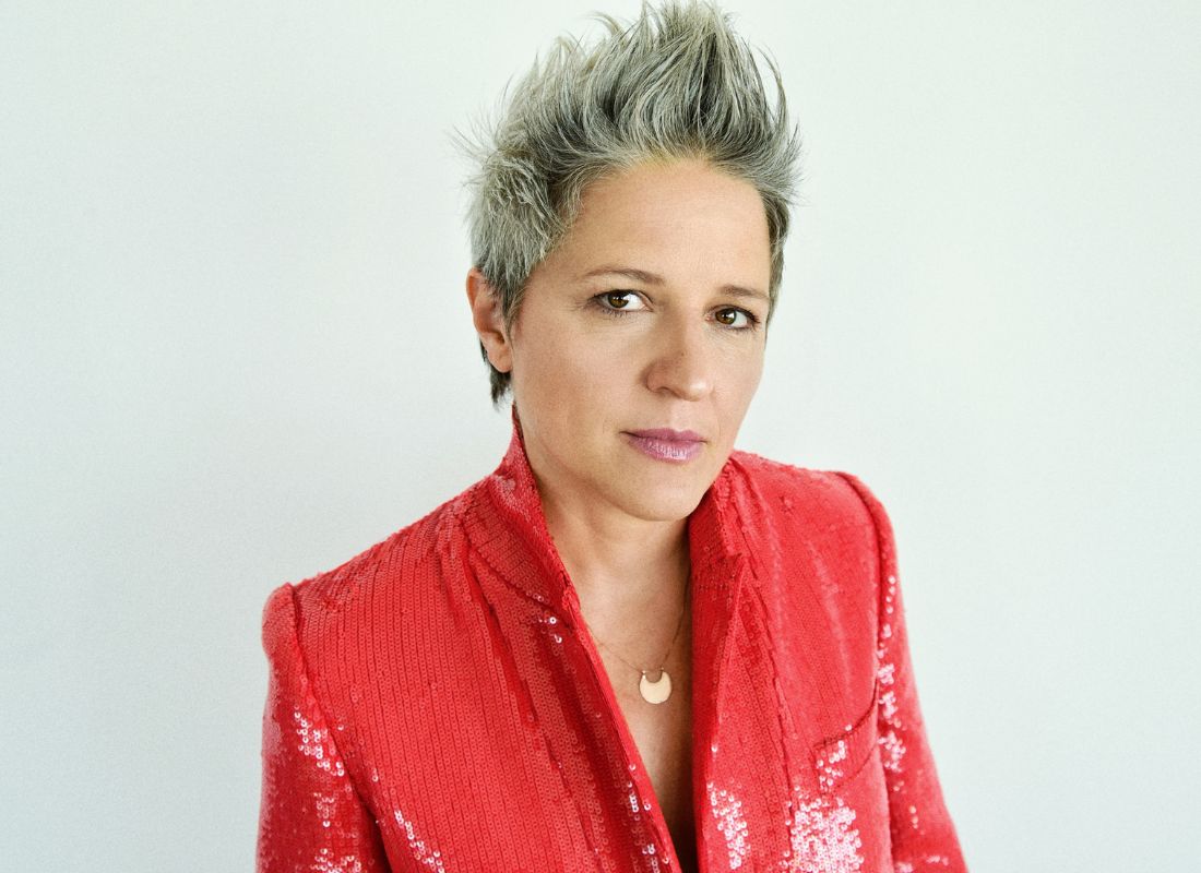 A woman in a red sequenced jack with short, pointed gray hair