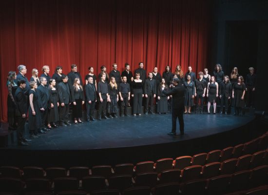 Photo of the PSU Chamber Choir singing on stage, conducted by Dr. Ethan Sperry