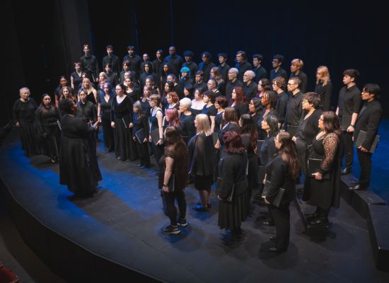 Photo of the Briar Choir singing on stage, conducted by Professor Coty Raven Morris.