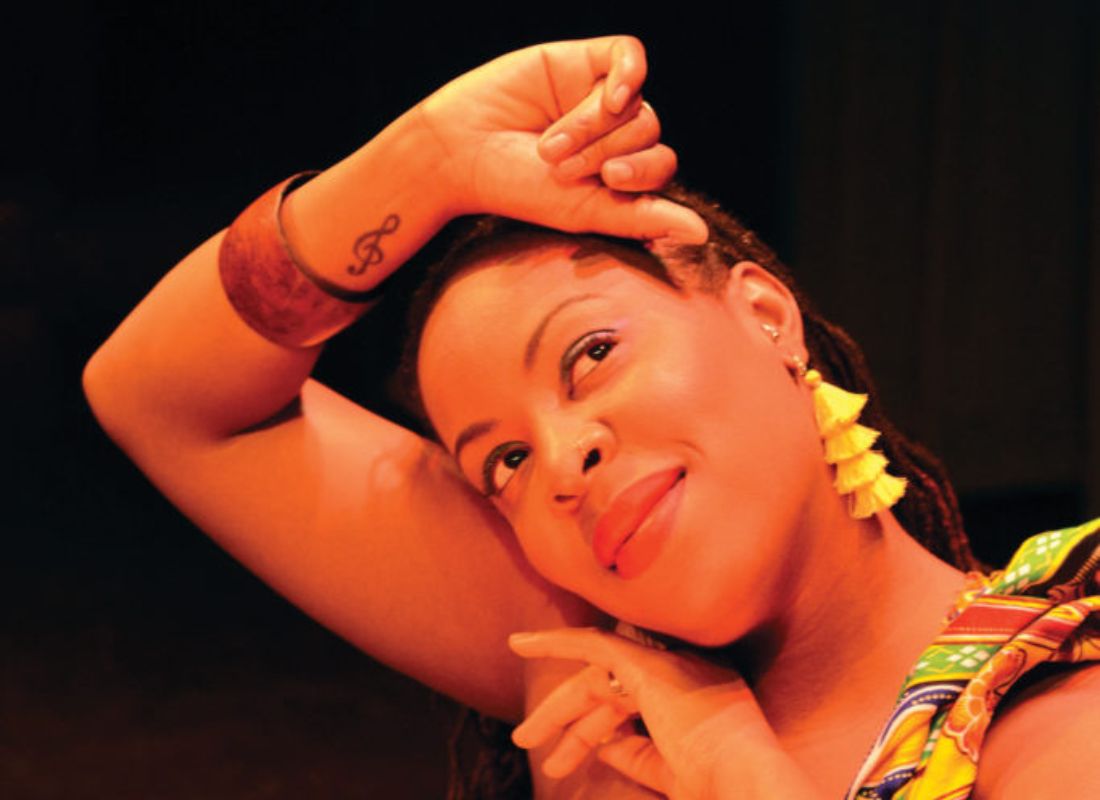 A woman with with her arm up and bent. She rests her head against the raised arm, and her other hand rests under her cheek