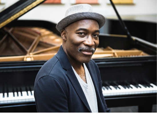 Headshot of PSU Jazz professor Darrell Grant sitting in front of a piano.