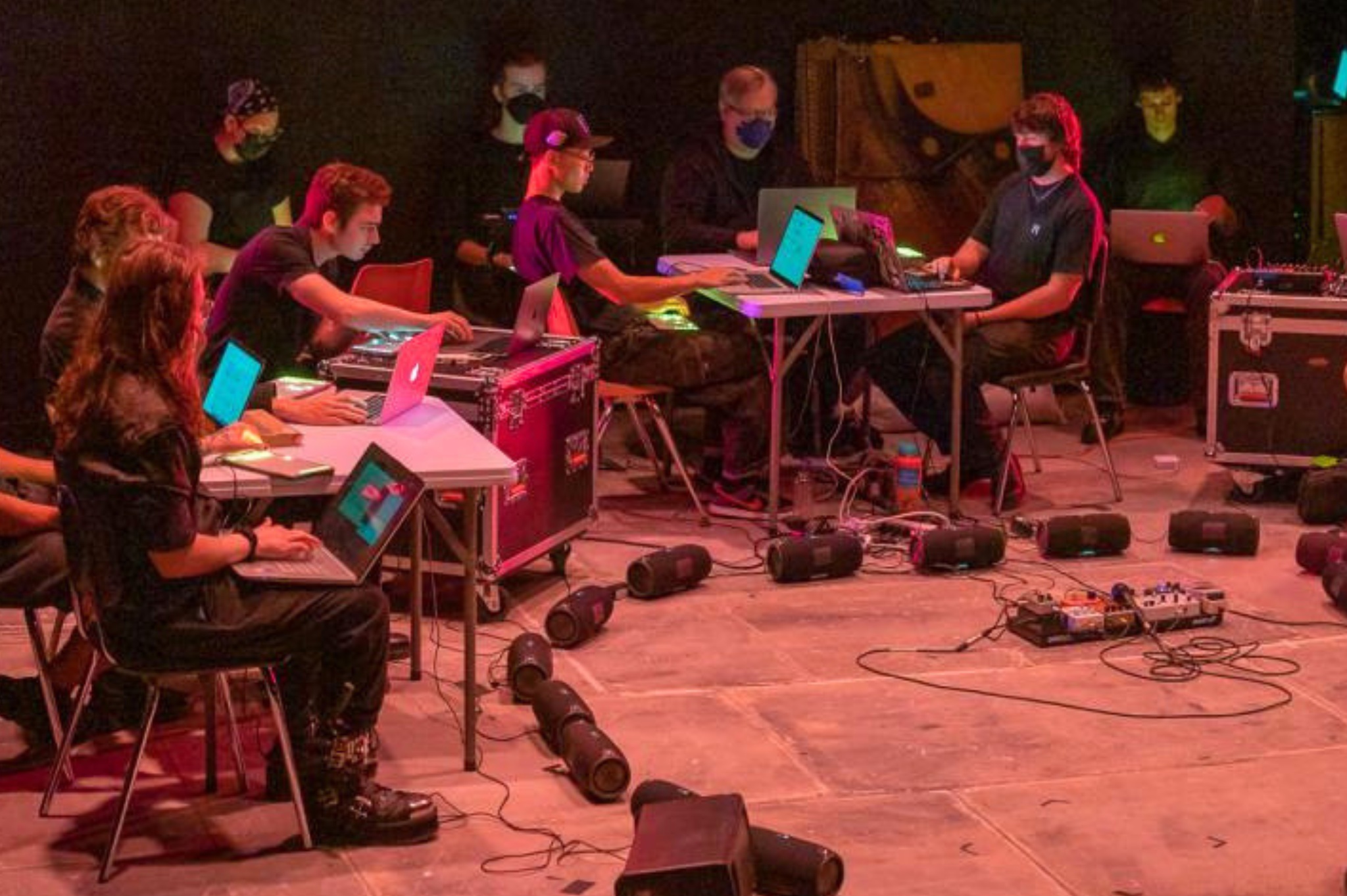 Students sitting at tables with laptops and midi controllers and speakers in a circle on the floor as they perform in the Laptop Ensemble. 