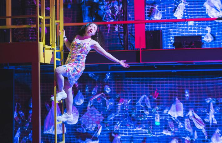 Actress leaning off a yellow ladder in PSU Theater's prodcution of "Frontieres sans Frontieres"
