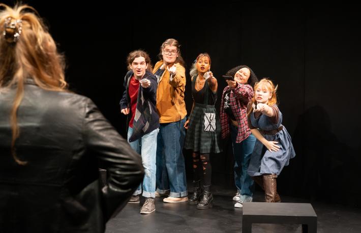 Five student actors reaching desperately towards a person whose back is to the camera, holding out money.