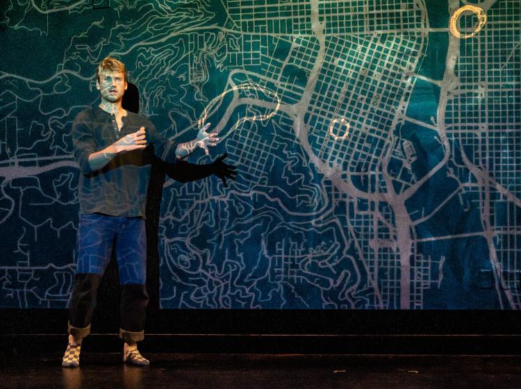 Actor with a map projected on him and the wall in PSU's Theater production of "Y/OURS."