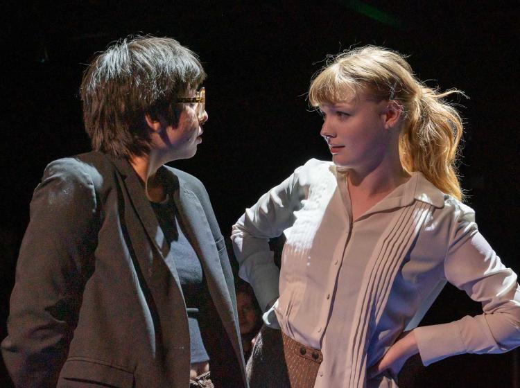 PSU cast perform in Caryl Churchill's "Love and Information." A close up of two characters looking into each other's eyes. The one's expression is subtly flirty and sassy.