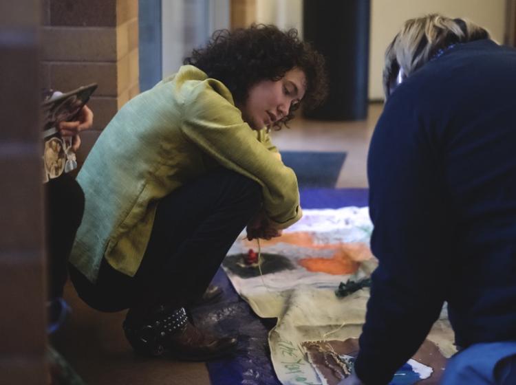 Students look at canvases of art laying on the floor.