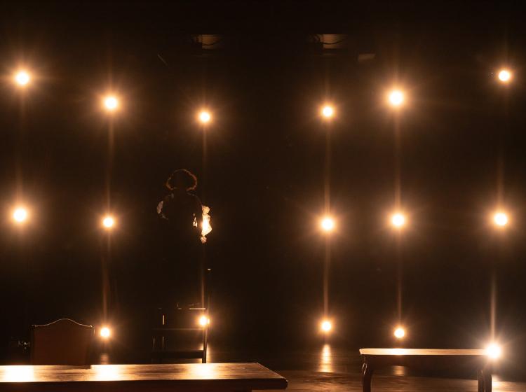 The silhouette of a woman can be faintly seen between the many lights that are shining towards the camera/audience.