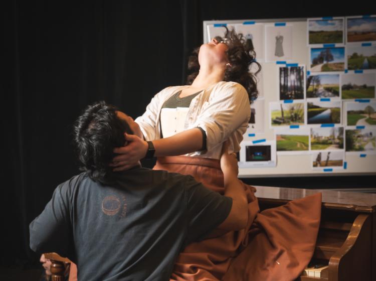 Woman sliding down a piano onto a man's lap straddling him with her corset showing and head thrown back.