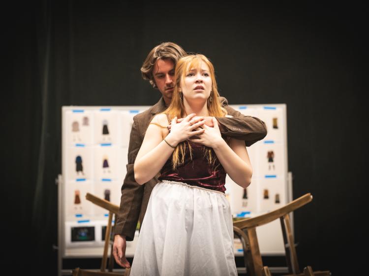 A young man stands behind a young woman who holds his hand on her chest.