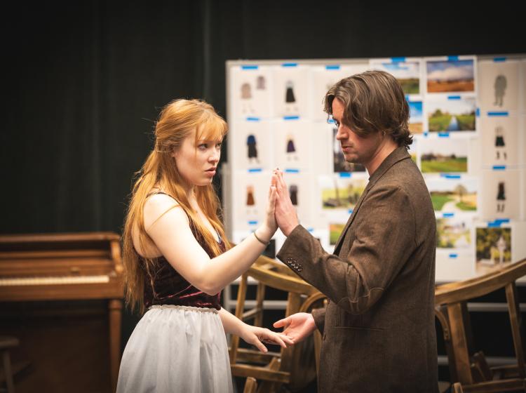A young woman and a young man hold stand in front of each other holding hands