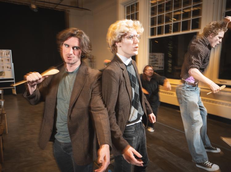 Two young men stand back two back in front of other young men rocking out.