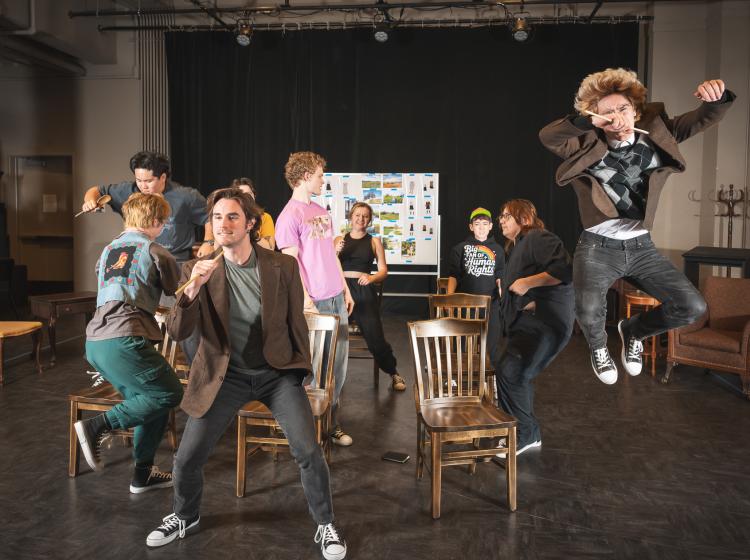A group of young men rocking out in a classroom, jumping from chairs.