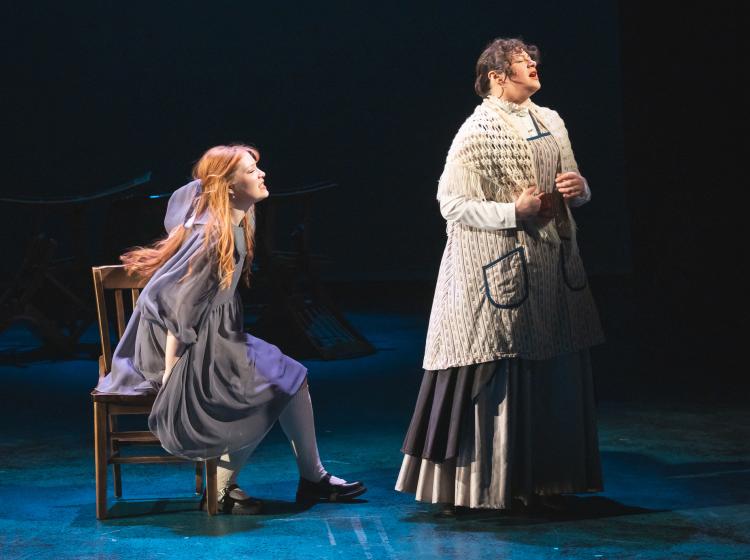 A young woman sitting on a chair and pleading to an older woman whose back is to her.