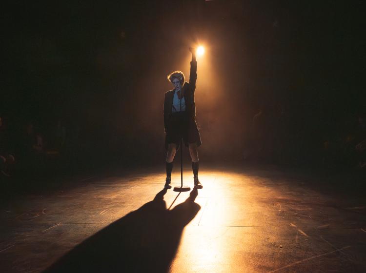Young man backlit by a spotlight standing at a microphone with his fist in the air .