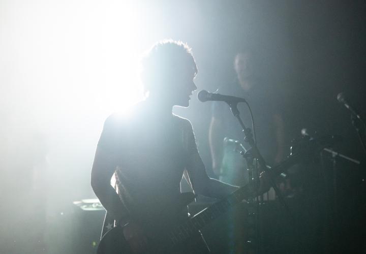 person with an electric guitar singing at a mic on stage 