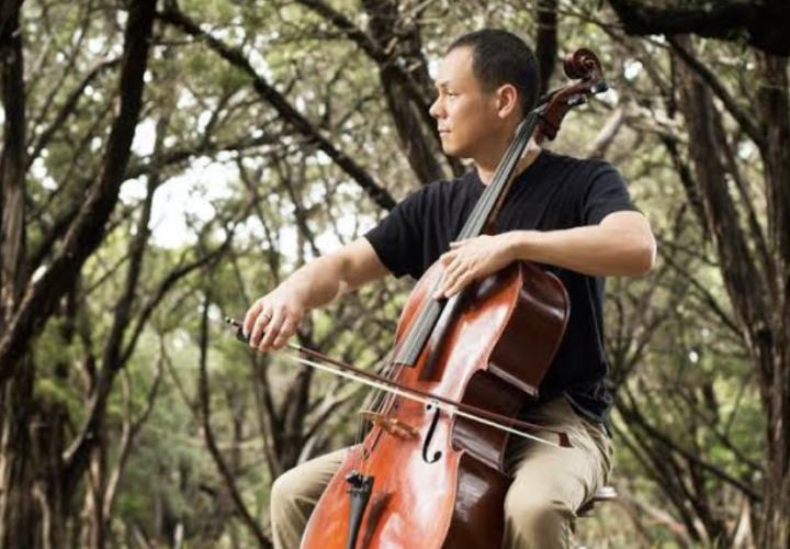 Headshot of cellist Bion Tsang in a forest.