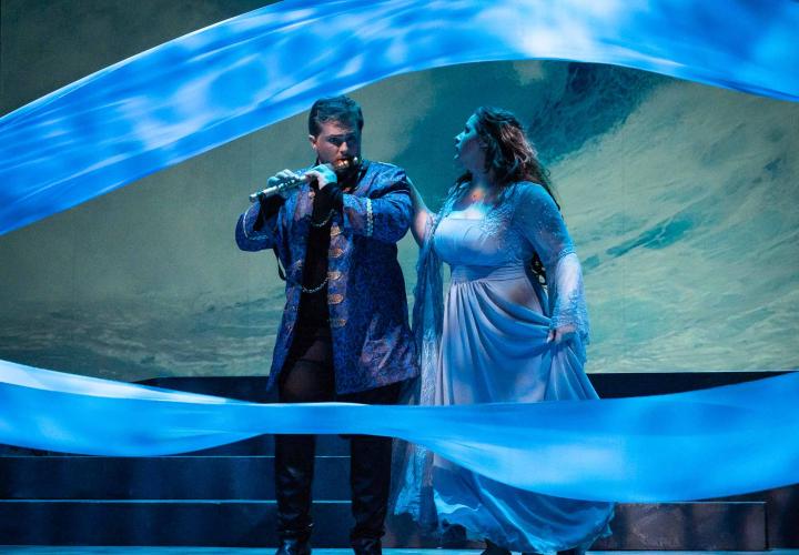 Scene from PSU Opera's "The Magic Flute." A performer playing the flute while passing through water colored scarves.