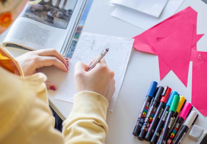 Photo of colored pens, colored paper cut into shapes, a magazine and a hand drawing or writing.
