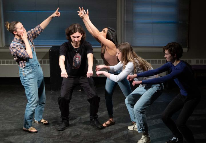 Five impro theater class students frozen in various animated gestures from an impro scene they are acting out.