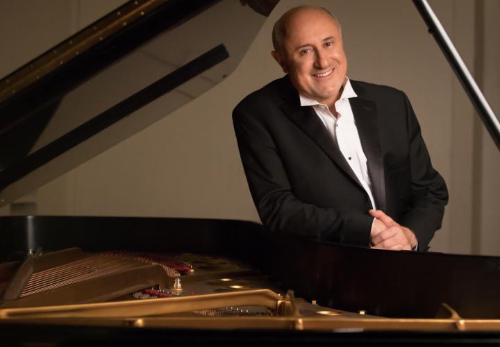 Headshot of PSU Steinway Piano Series guest artist Dmitry Rachmanov leaning on an open grand piano.