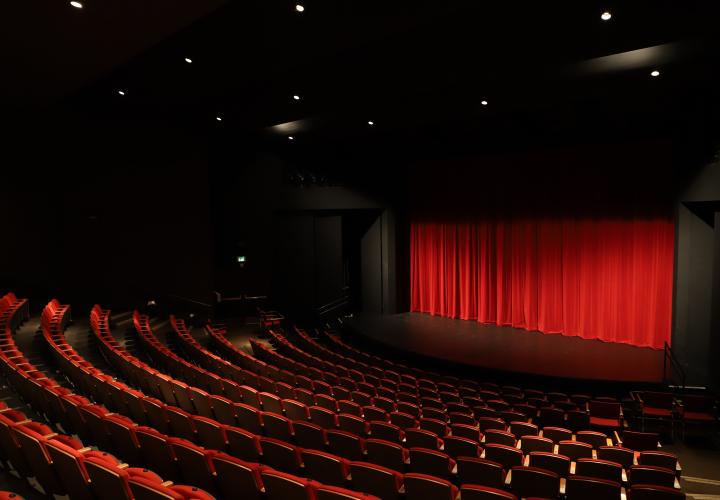 Photo of Portland State University's Lincoln Performance Hall stage with red curtain drawn. Taken from the back of the auditorium so that the rows of red seats can be seen.