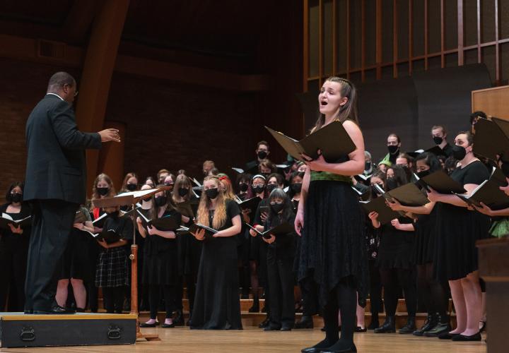 Choir student singing a solo with the choir behind them.