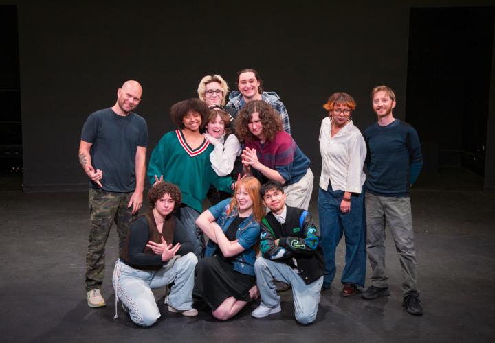 Members of the PSU Impro Ensemble grouped against a black stage smiling.