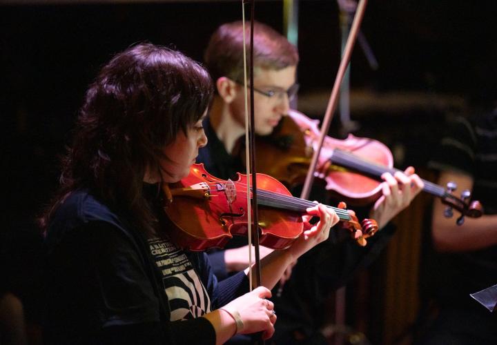 Two students playing violin on a dimly lit stage.