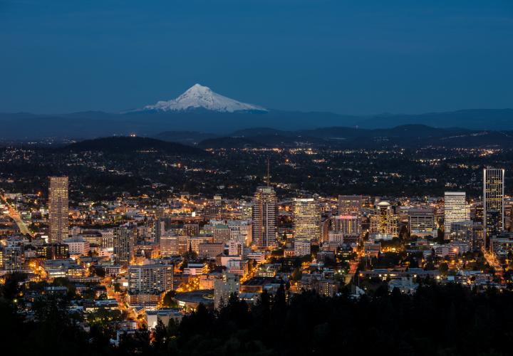 Hilltop view of Portland city lit up at night with Mt. Hood in the background.