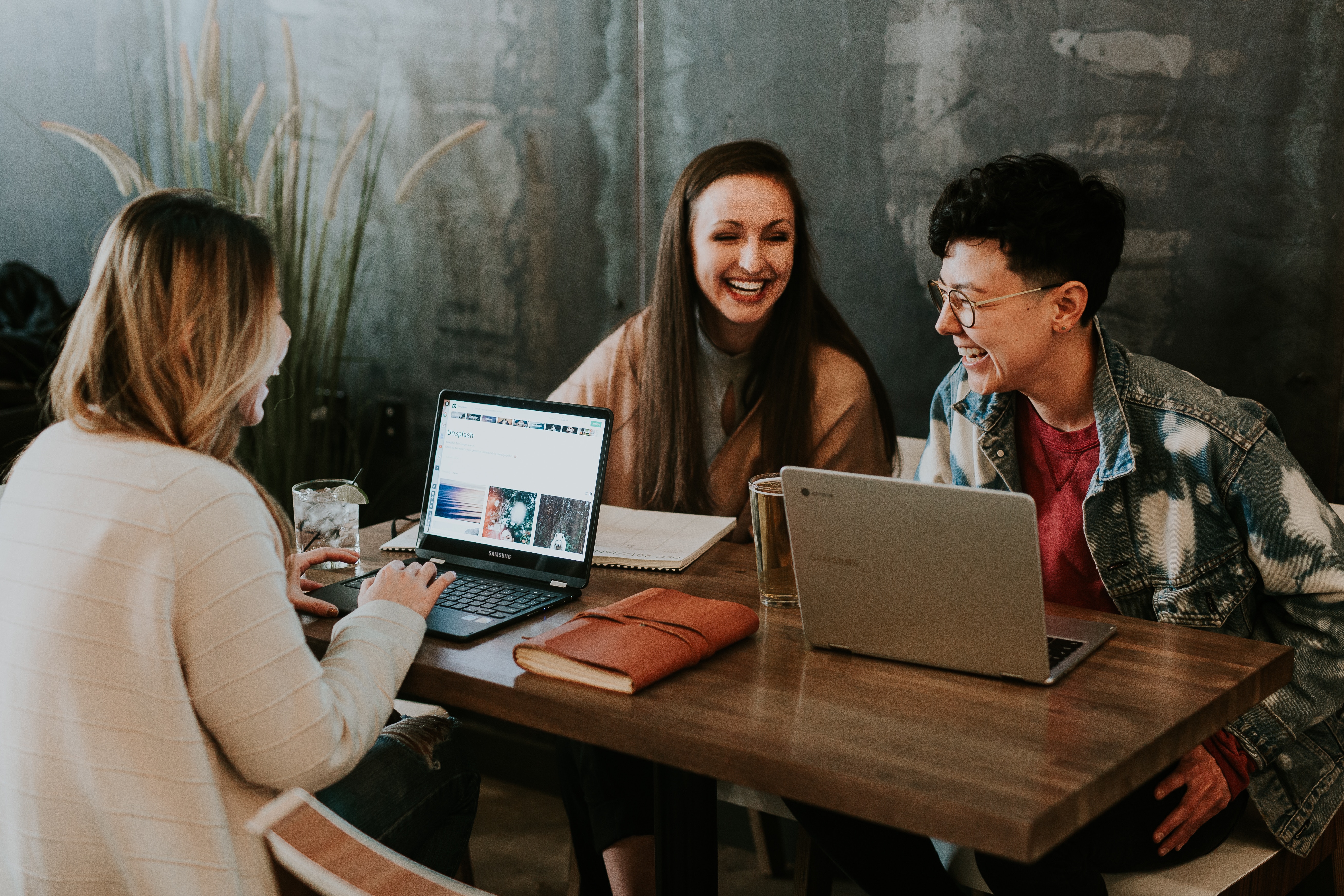 three people sitting at a table with their laptops working and laughing