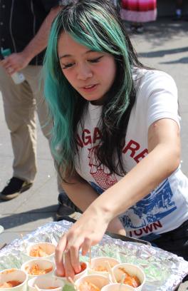 picture of a person with black and turquoise hair serving salmon in small cups