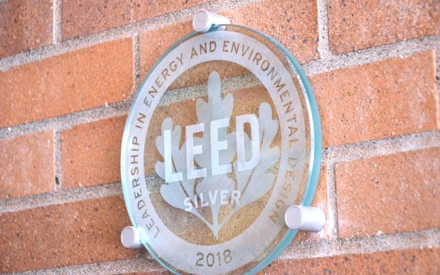 picture of a glass circle with the words "Leadership energy and environmental design 2018" and LEED silver on a brick wall