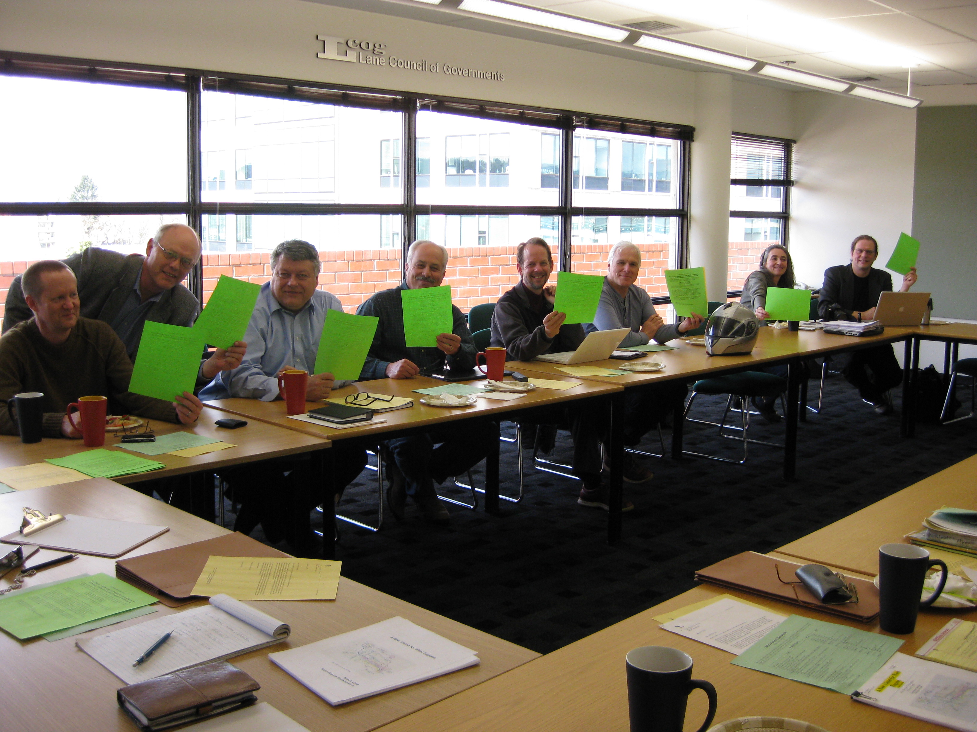 A group of folks sitting around a table, holding green pieces of paper to show their consensus