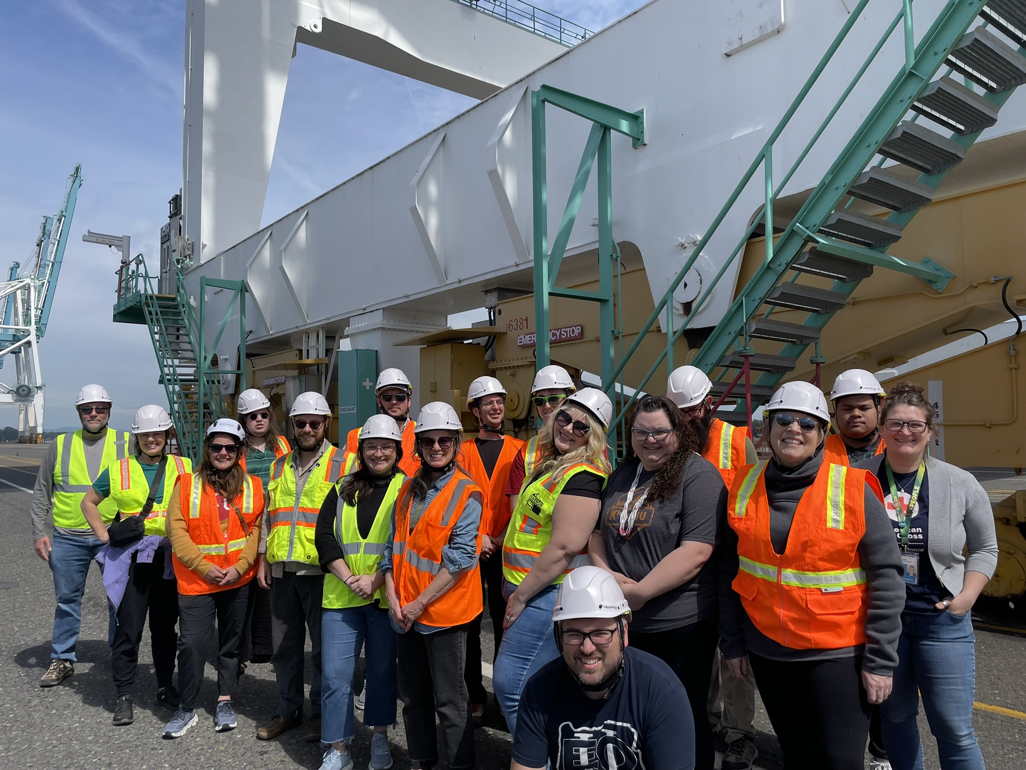 Group of students wearing orange reflective vests and white hardhats, standing together and smiling at the camera