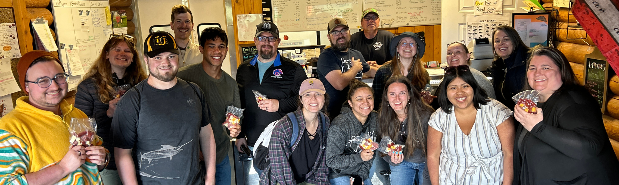 A group of PSU and Eastern Oregon University students grouped together in a butcher shop in Eastern Oregon as part of the Urban Rural Ambassador course. Everyone is smiling, looking at the camera