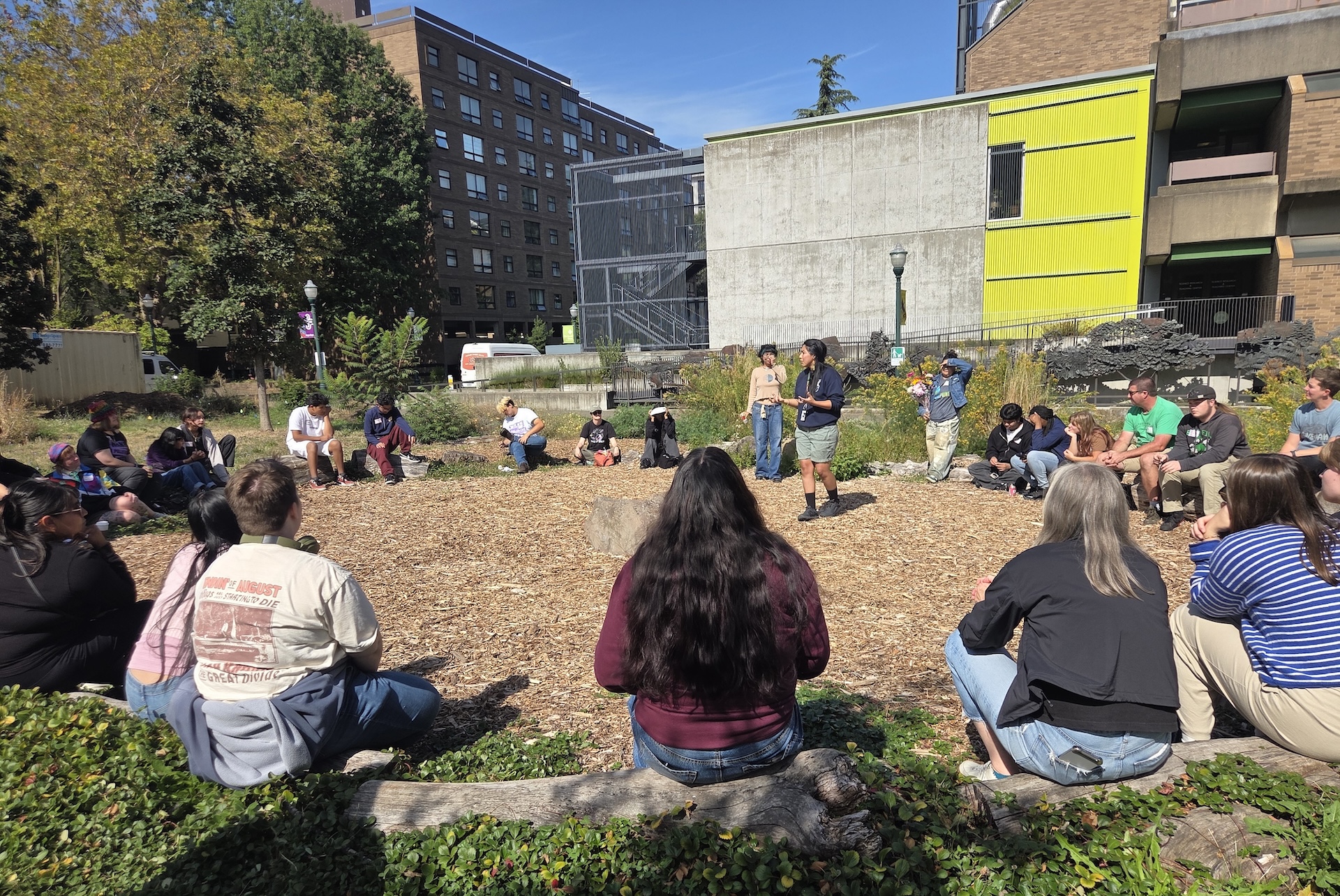 Participants sit in a large circle outdoors in the PSU Oak Savanna as a presenter in the middle teaches them about the Indigenous Traditional Ecological & Cultural Knowledge (ITECK) Center.