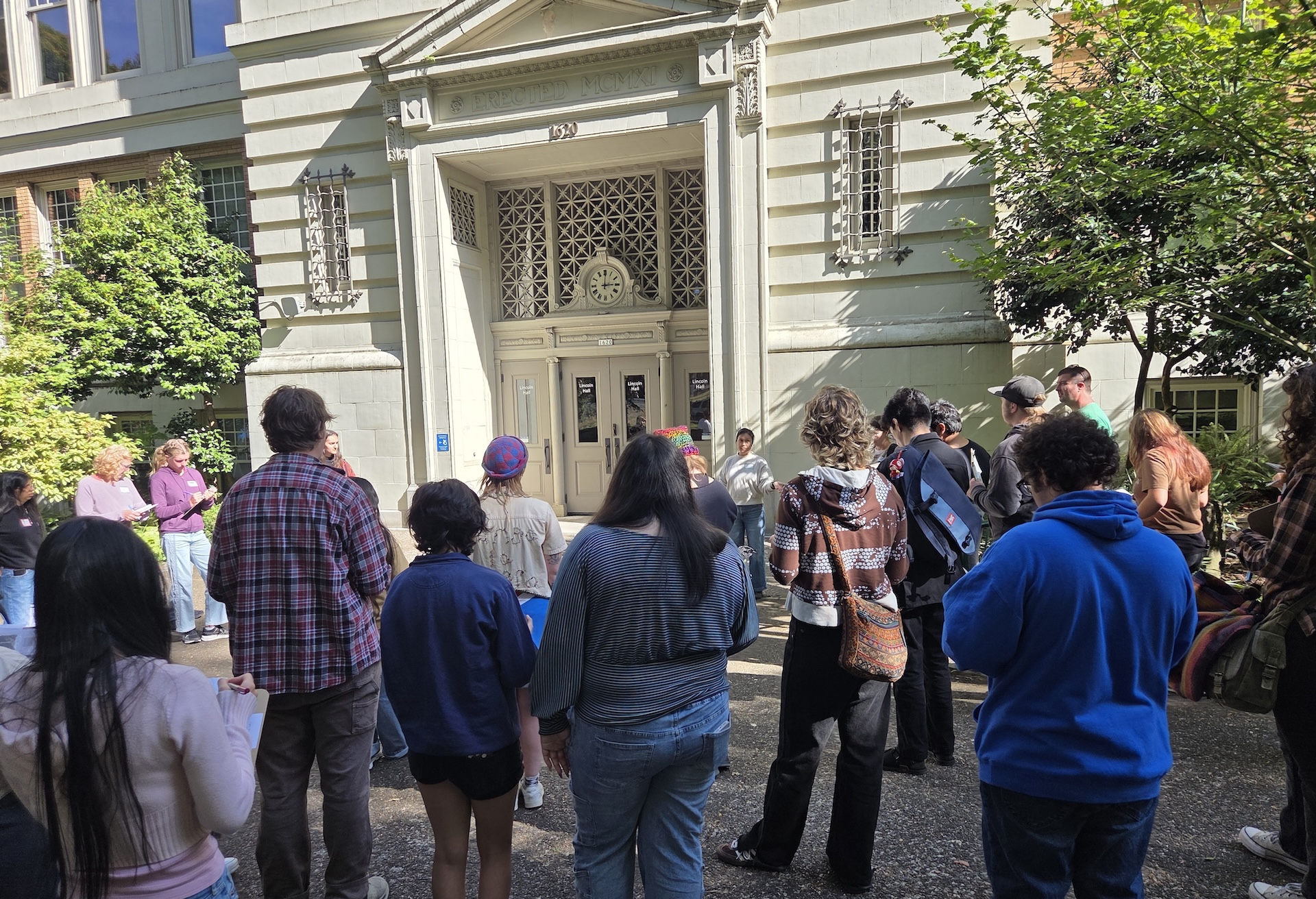 Participants gather around a building while being guided on a mapping tour.