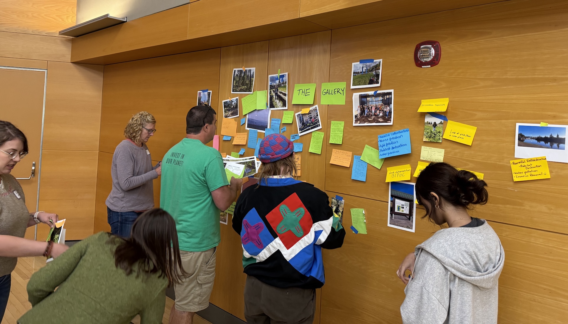Participants gather around to create a photo gallery by sticking notecards and photos to a wall to illustrate issues and solutions in their communities.