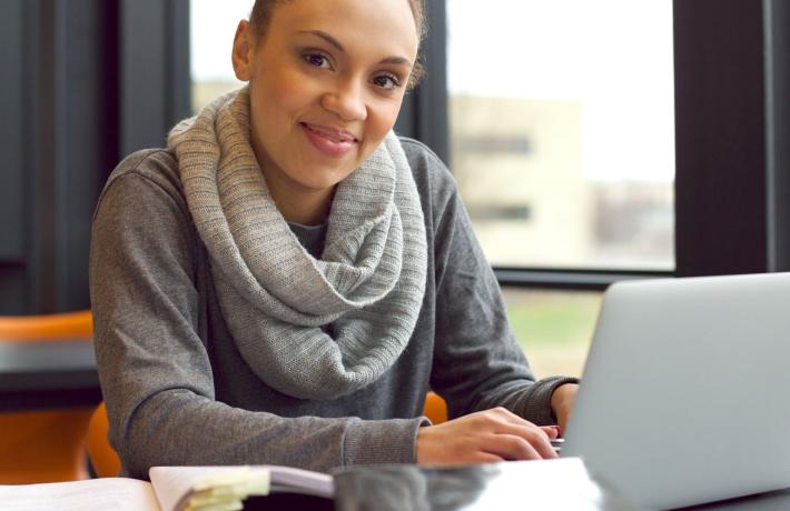 Woman doing research with computer and stack of books