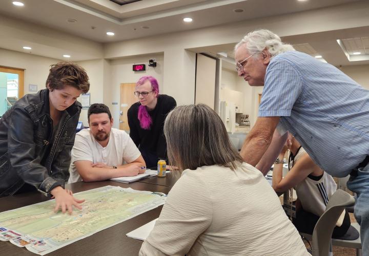 Participants of the 2025 Albany Civic Leadership Academy is sitting and standing around a table, reviewing a map together.