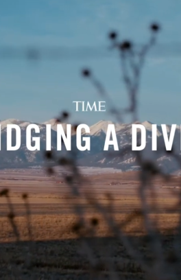 Still frame from the Time Magazine video entitled, "Bridging a Divide." Behind the white text of the title is the eastern Oregon wilderness, with a long field and mountains in the background.