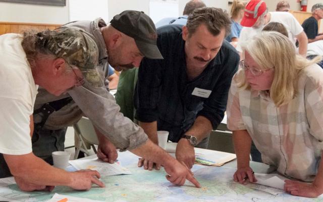A group of people leaning over a map and pointing at different areas