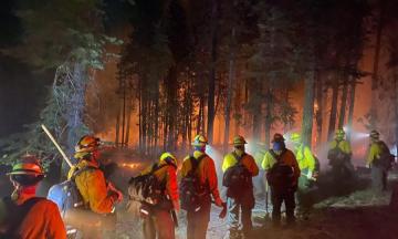 Oregon firefighters approaching a forest with a red-orange glow of the fire around it.